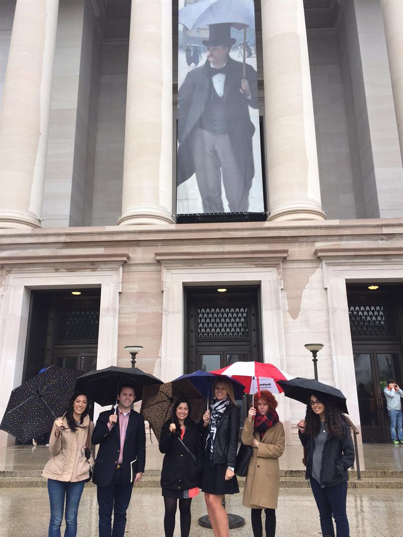 Six students with umbrellas standing in front of the entrance to the Caillebotte exhibition in Washington