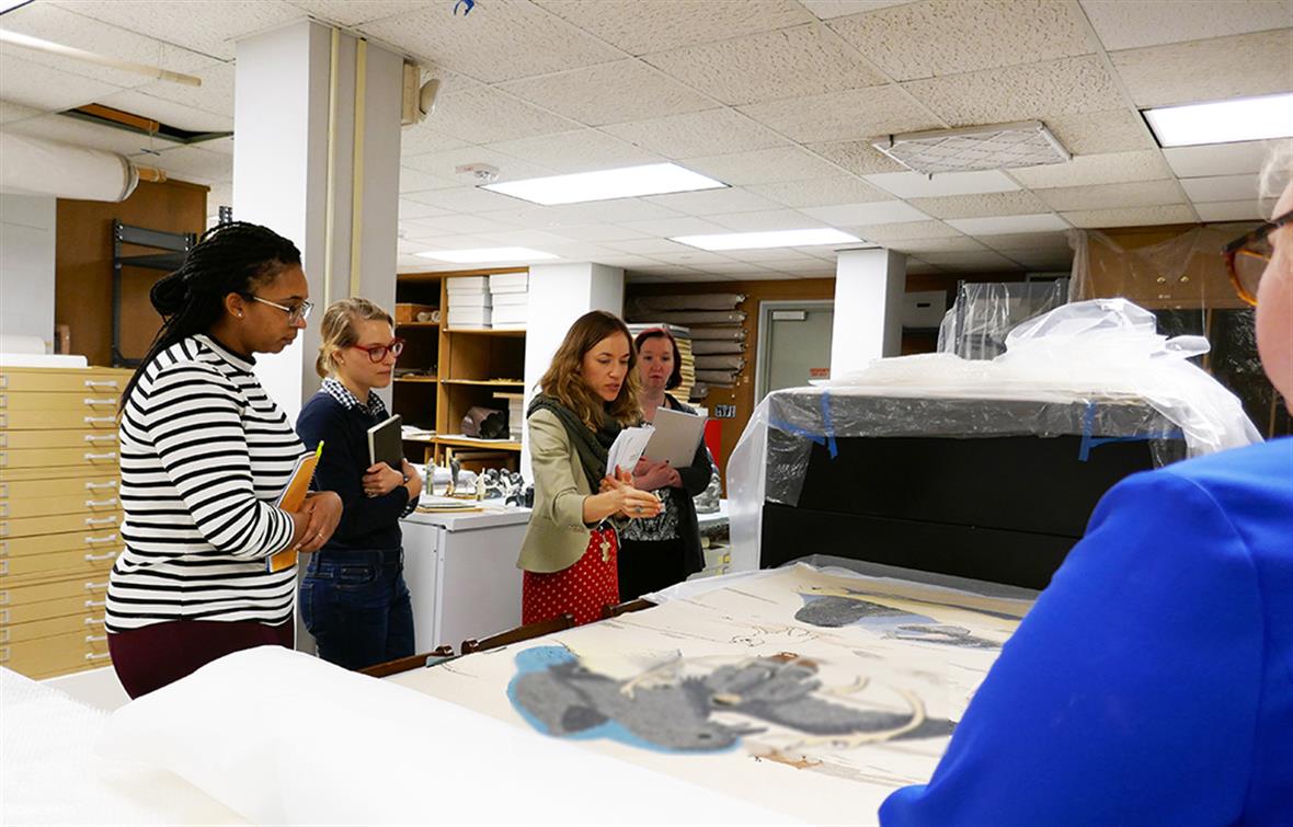 Prof. Jessica Horton and students in the Museums storage facility looking at a large tapestry and discussing the work. 