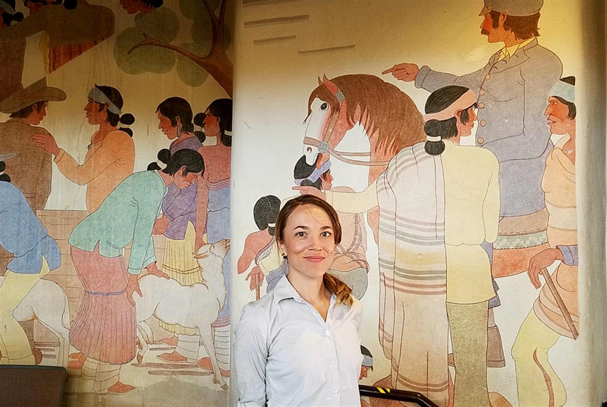 Jessica Horton standing in front of a mural featuring native peoples